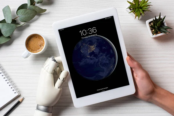 Cropped image of businessman with prosthesis hand using ipad at table with coffee cup in office — Stock Photo