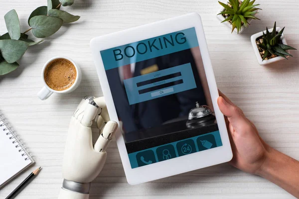 Partial view of man with prosthesis arm using digital tablet with booking on screen at table with coffee cup in office — Stock Photo