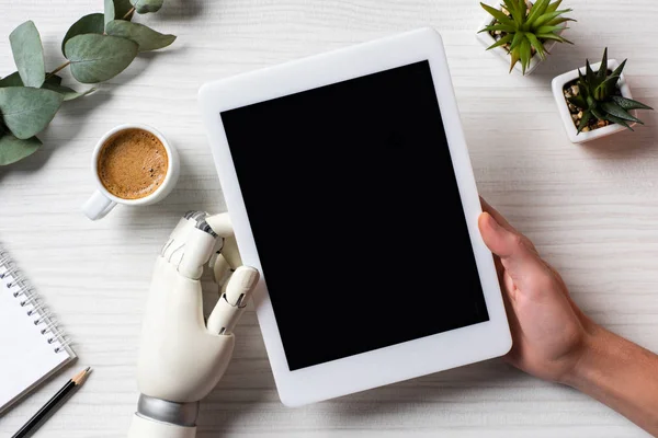 Vista parcial del hombre de negocios con brazo de prótesis utilizando tableta digital con pantalla en blanco en la mesa con taza de café en la oficina - foto de stock