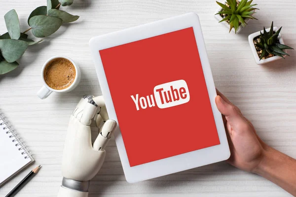 Cropped image of man with prosthesis arm using digital tablet with youtube on screen at table with coffee cup in office — Stock Photo