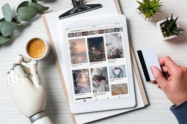 Vue partielle de l'homme d'affaires avec prothèse main tenant la carte de crédit et en utilisant une tablette numérique avec infographie à l'écran à la table avec tasse à café dans le bureau — Photo de stock