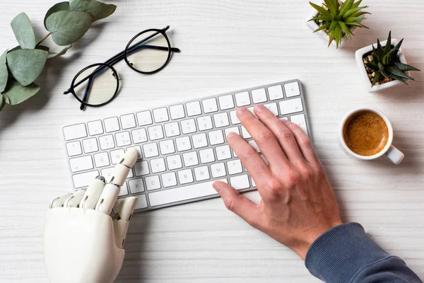 Обрезанный образ бизнеса с протезной рукой, печатающей на клавиатуре компьютера за столом в офисе — стоковое фото
