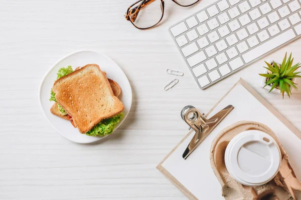 Elevated view of paper coffee cup, sandwich and computer keyboard at table in office — Stock Photo