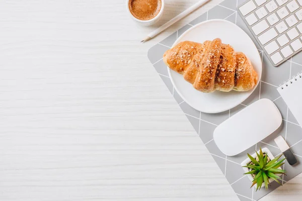 Vue de dessus du lieu de travail avec croissant arrangé, tasse à café et clavier d'ordinateur dans le bureau — Photo de stock