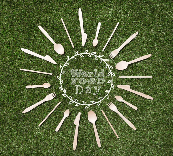 Vista superior de colheres de madeira com garfos e facas em forma de sol deitado na grama, inscrição dia mundial da comida — Fotografia de Stock