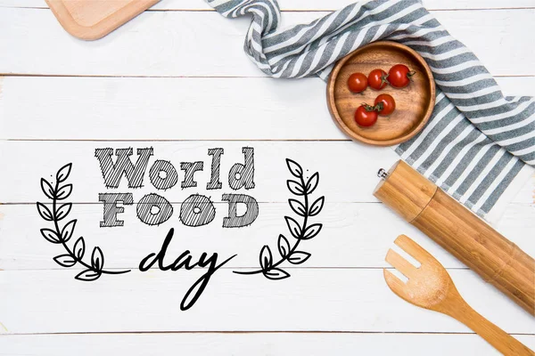 Tomates cherry con espátula de madera y molinillo de sal con mantel en la mesa, inscripción del día mundial de la comida - foto de stock