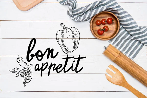 Tomates cerises avec spatule en bois et moulin à sel avec nappe sur la table, inscription bon appétit — Photo de stock