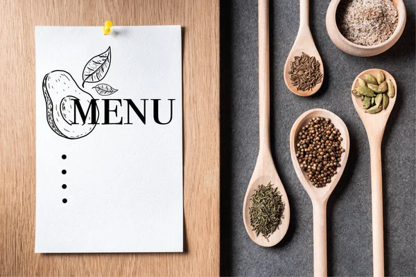 Top view of dried spices on wooden spoons and paper sheet with menu inscription — Stock Photo