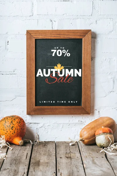 Close up view of raw pumpkins on wooden tabletop and chalkboard with autumn sale inscription hanging on white brick wall — Stock Photo
