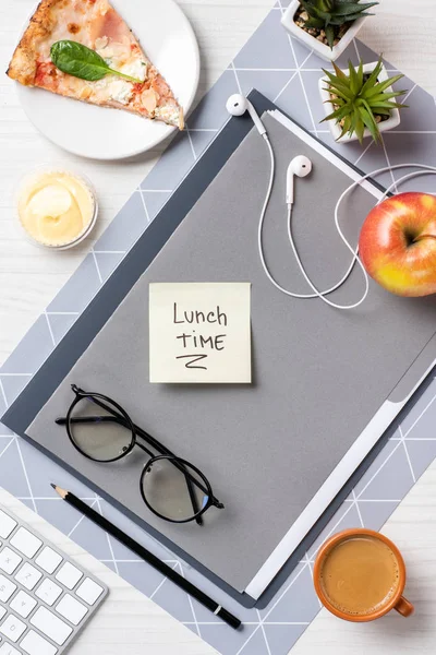 Top view of sticky note with inscription lunch time, eyeglasses, earphones, pizza an apple on table — Stock Photo