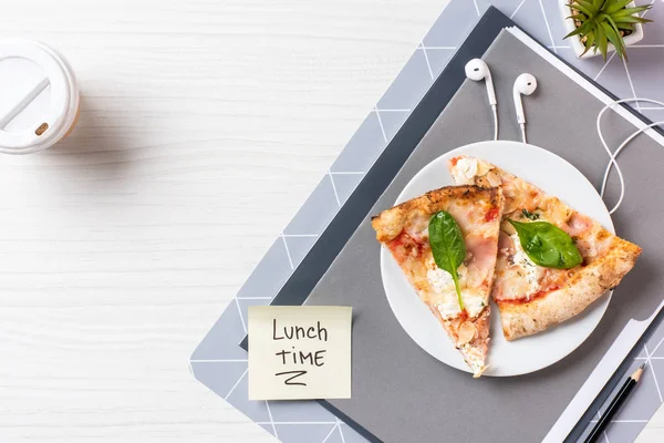 Von oben: Haftnotiz mit Aufschrift Mittagszeit, Kopfhörer und Pizza auf dem Tisch — Stockfoto