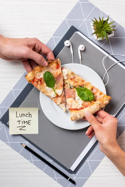 Partial top view of people holding pizza pieces above white plate in office — Stock Photo