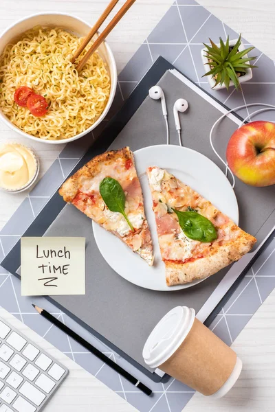 Top view of pizza, noodles, apple, disposable coffee cup and lunch time inscription on paper at workplace — Stock Photo