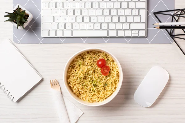 Top view of bowl with noodles, fork, computer mouse and keyboard at workplace — Stock Photo