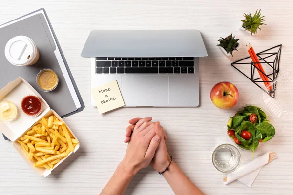 Partial top view of female hands, laptop, note with inscription make a choice and healthy food with junk food at workplace — Stock Photo