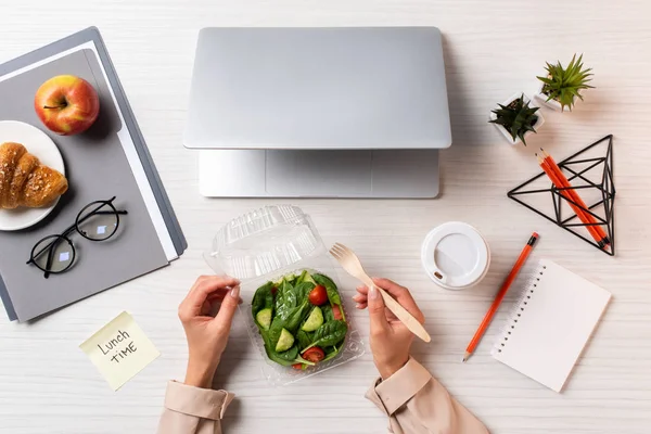 Colpo ritagliato di persona che mangia insalata di verdure sul posto di lavoro con laptop e forniture per ufficio — Foto stock