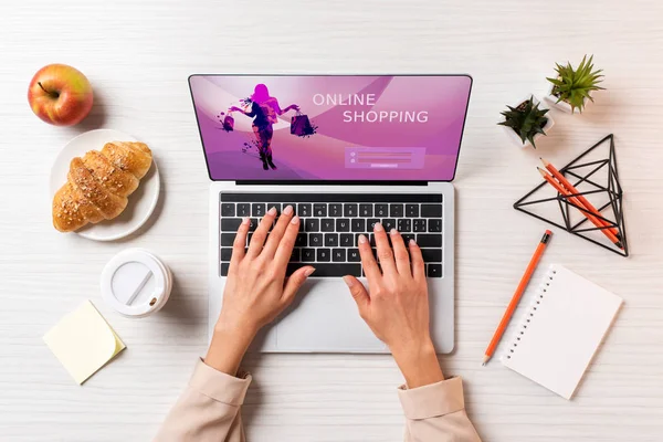 Cropped shot of businesswoman using laptop with online shopping website at table with coffee, apple and croissant — Stock Photo