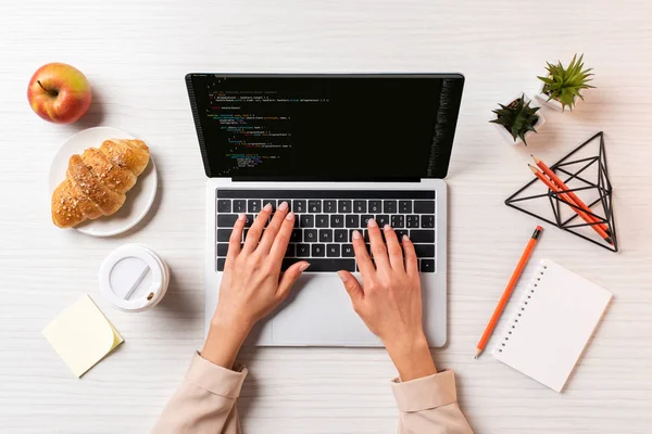 Cropped shot of businesswoman using laptop with html code on screen at table with coffee, apple and croissant — Stock Photo