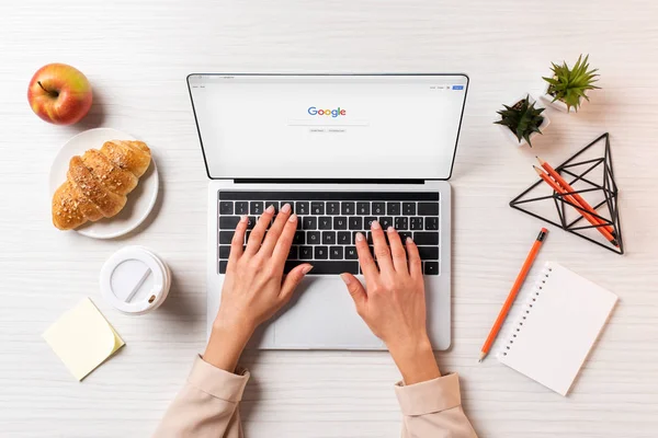 Tiro cortado de empresária usando laptop com o site do Google na mesa com café, maçã e croissant — Fotografia de Stock