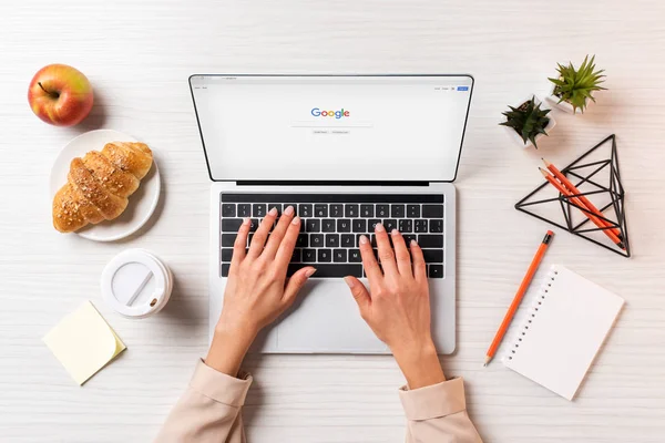 Cropped shot of businesswoman using laptop with google website at table with coffee, apple and croissant — Stock Photo