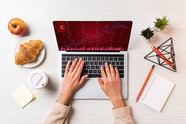 Tiro recortado de la mujer de negocios utilizando el ordenador portátil con gráficos en la mesa con café, manzana y croissant - foto de stock