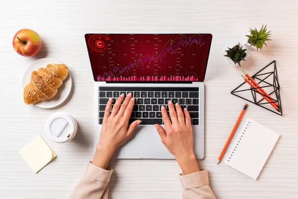 Colpo ritagliato di donna d'affari utilizzando laptop con grafici a tavola con caffè, mela e croissant — Stock Photo