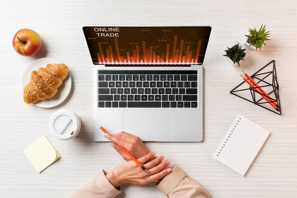 Cropped shot of female hands, laptop with online trade graphs and lunch on table in office — Stock Photo