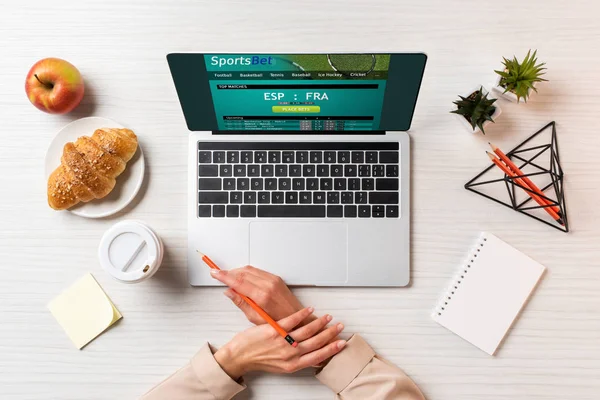 Обрезанный снимок женских рук, ноутбук с веб-сайтом спортивной ставки и ланч на столе в офисе — стоковое фото