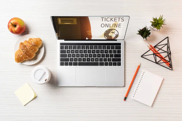 Vue du dessus de l'ordinateur portable avec billets site web en ligne, tasse en papier, pomme et croissant sur la table au bureau — Photo de stock