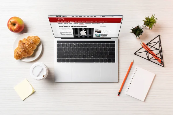 Top view of laptop with bbc news website, croissant and coffee to go on office table — Stock Photo