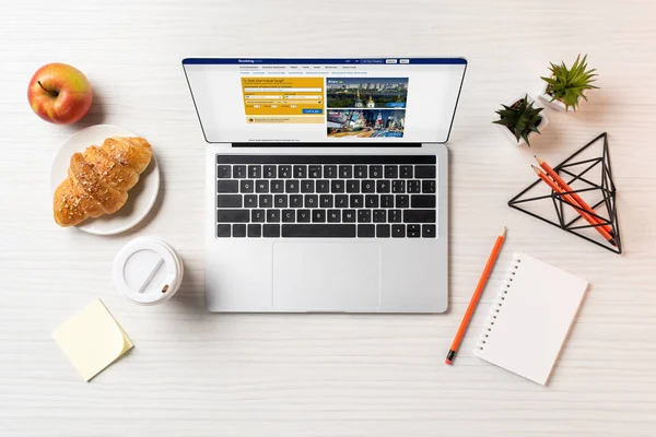 Top view of laptop with booking website, croissant and coffee to go on office table — Stock Photo