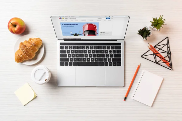 Laptop von oben mit ebay-Website, Croissant und Kaffee to go auf dem Bürotisch — Stockfoto