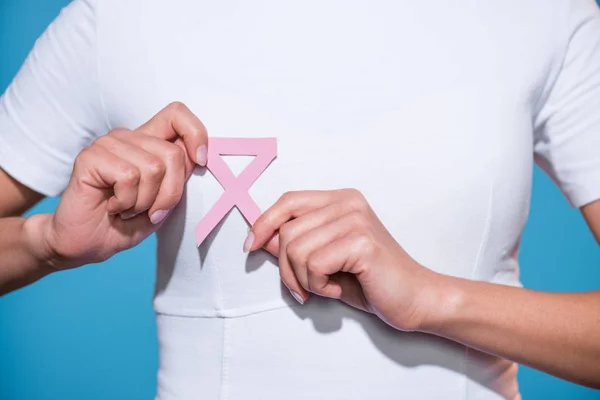 Vista parziale della donna che tiene il cancro al seno consapevolezza nastro rosa su sfondo blu — Foto stock