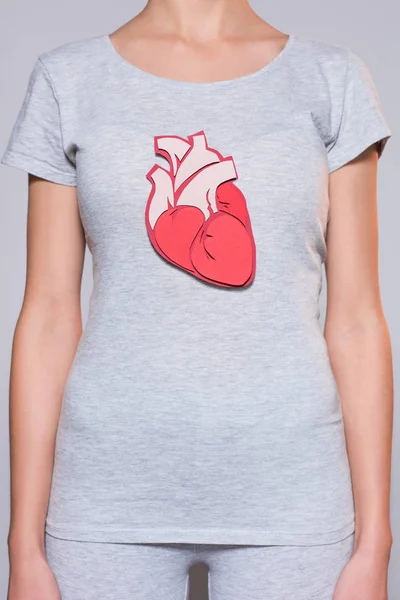 Vista parcial de la mujer con el corazón hecho a mano de papel en la camiseta sobre fondo gris - foto de stock