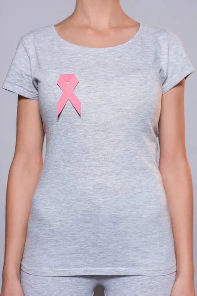 Tiro recortado de mujer en camiseta gris con el cáncer de mama conocimiento cinta rosa sobre fondo gris - foto de stock