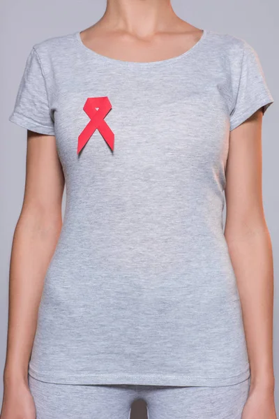 Cropped shot of woman in grey tshirt with aids prevention red ribbon on grey background — Stock Photo