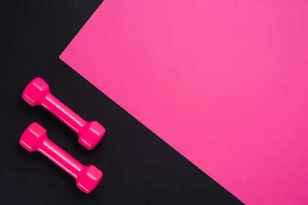 Flat lay with two dumbbells on pink and black background with copy space — Stock Photo