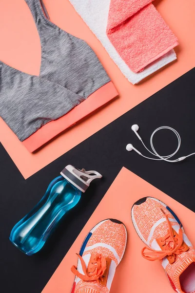 Vista superior de zapatillas, mancuernas, botella deportiva, toalla, ropa deportiva y auriculares sobre fondo negro - foto de stock