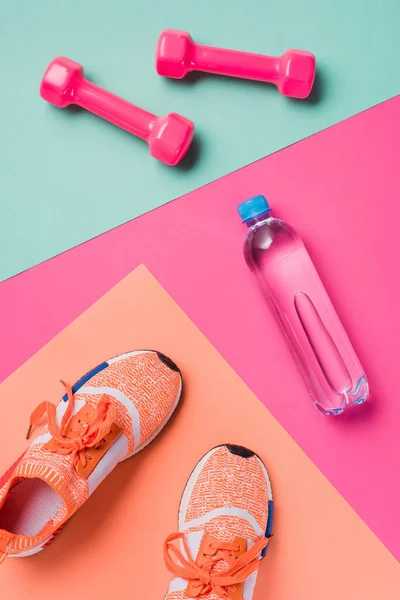 Piso con zapatillas de deporte, mancuernas y botella de deporte sobre un fondo colorido — Stock Photo