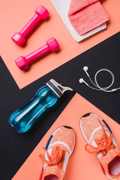 Pose plate avec baskets, haltères, bouteille de sport, serviette et écouteurs sur fond noir — Photo de stock