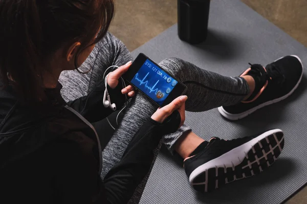 Vue recadrée d'une femme sportive tenant un smartphone avec son pouls à l'écran — Photo de stock