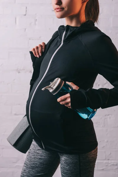 Vista recortada de la mujer embarazada atlética con esterilla deportiva y botella de agua - foto de stock