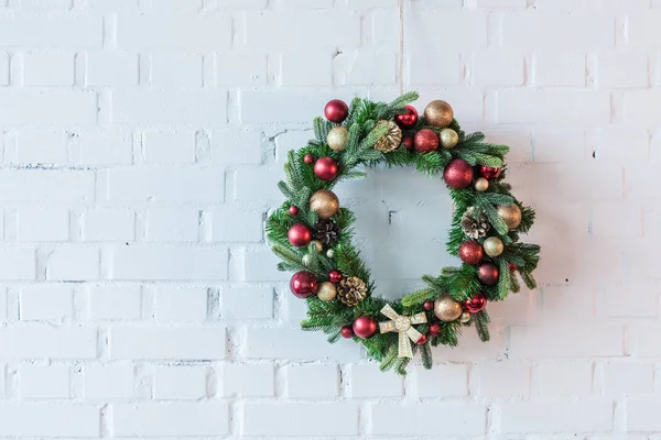 Corona de Navidad decorada con bolas y arco en el fondo de la pared de ladrillo blanco — Stock Photo