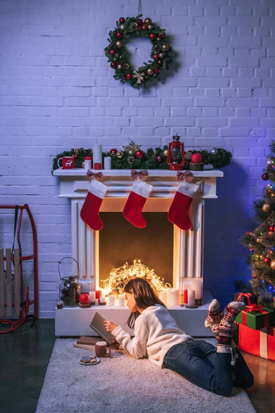 Entzückende Frau liest in der Nähe von weihnachtlich geschmücktem Kamin und Weihnachtsbaum — Stockfoto