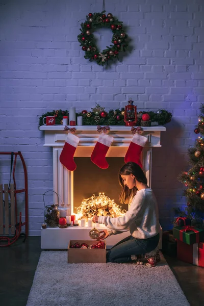 Schöne Frau sitzt neben geschmücktem Kamin und Weihnachtsbaum — Stockfoto
