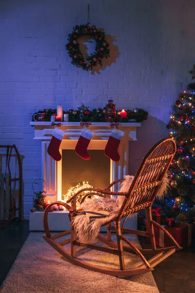 Камин с рождественскими украшениями возле елки и деревянного кресла-качалки — стоковое фото