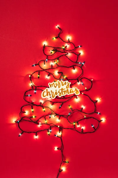 Цветные гирлянды в виде рождественской ёлки с рождественской вывеской на красном фоне — стоковое фото