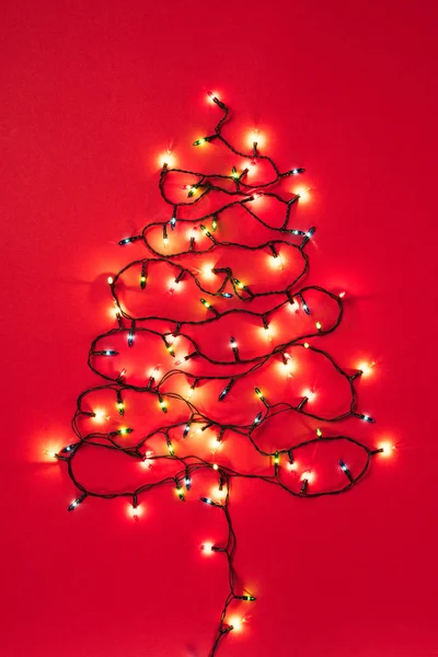 Bunte Girlanden in Form eines Weihnachtsbaums auf rotem Hintergrund — Stockfoto