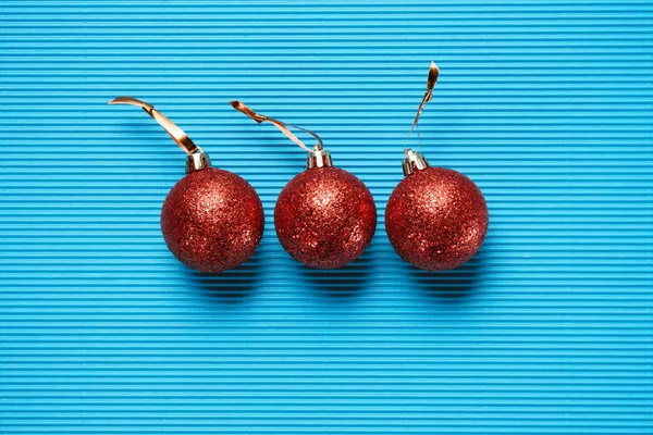 Colocación plana de tres bolas de Navidad decorativas brillantes rojas sobre fondo azul texturizado - foto de stock