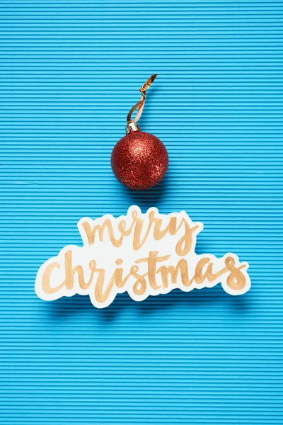 Flat lay of Merry Christmas sign and christmas ball on the blue textured background — Stock Photo